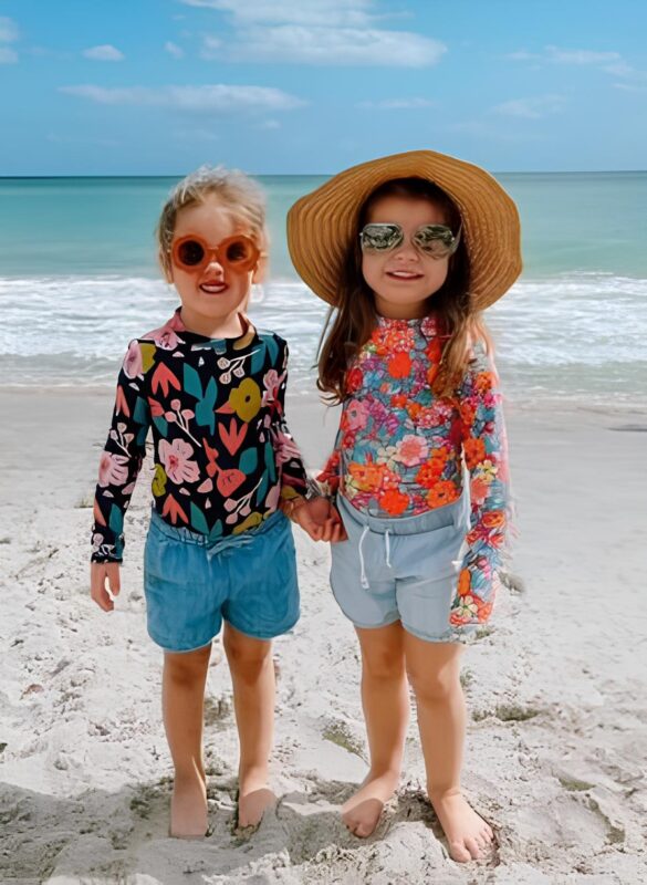 Two girls on beach wearing floral shirts.