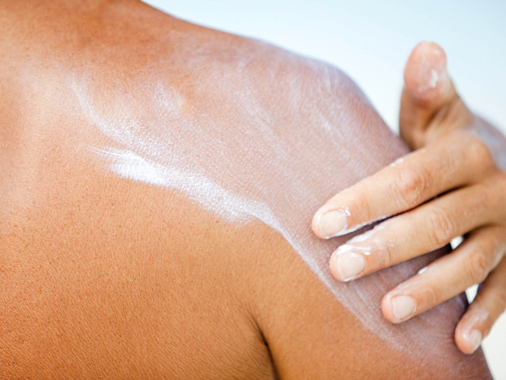 Hand applying sunscreen to shoulder.